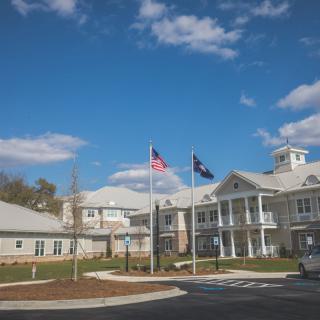 A white building with flags flying in front, set against a blue sky with scattered clouds.