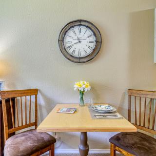 A cozy dining nook featuring a wooden table with two chairs, adorned with a floral centerpiece and set beneath a stylish wall clock.