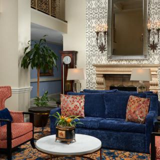A cozy living room with a blue sofa, patterned throw pillows, and a fireplace featuring an ornate mirror above it.