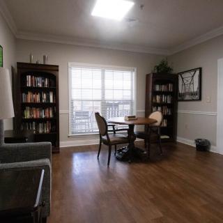 A cozy reading room with bookshelves, a table, and chairs by a large window.