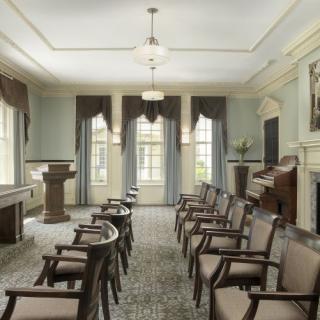 A quiet meeting room with arranged chairs, a lectern, and large windows with curtains.