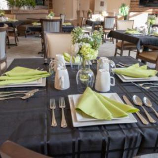 An elegantly set dining table in a restaurant with green napkins and floral centerpiece.