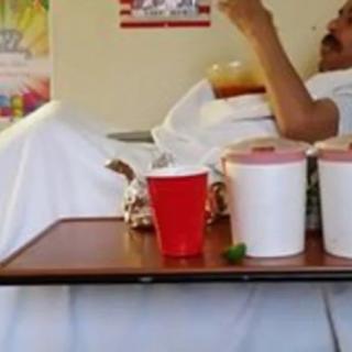 A patient in a hospital bed with a food tray holding drinks and containers.