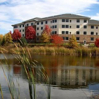 A building surrounded by autumn trees reflected in a nearby lake.