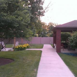 A tranquil garden with a paved pathway leading to a gazebo, surrounded by trees and flowers.