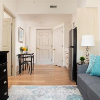 A cozy living space with modern decor, featuring a sofa, lamp, small dining table, and wooden flooring.