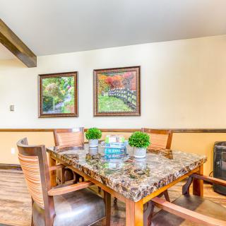 A cozy dining area with a marble top table, surrounded by wooden chairs and decorated with small plants and framed artwork.
