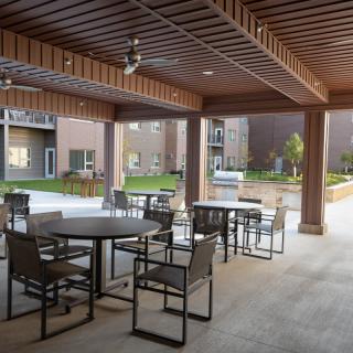 A covered patio area with tables and chairs overlooking a garden in an apartment complex.