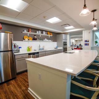 A modern kitchen interior featuring stainless steel appliances and a large white countertop with bar stools.