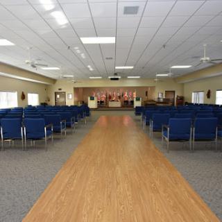 A spacious empty hall with blue chairs arranged in rows, leading towards a stage area.