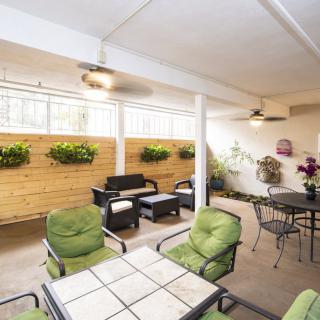 A cozy indoor patio with comfortable seating, green cushioned chairs, and plants adorning the walls.