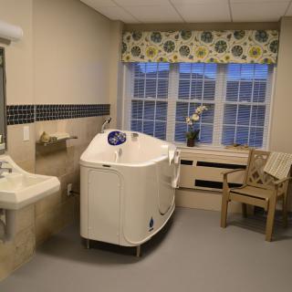 A well-lit bathroom with a bathtub, sink, chair, and large window.