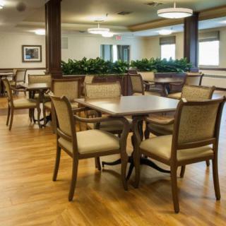 A well-lit dining area with wooden flooring, featuring tables and chairs arranged neatly.