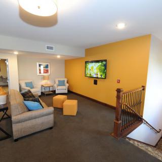A modern living room with a comfortable sofa, chairs, and a wall-mounted television on a yellow accent wall.