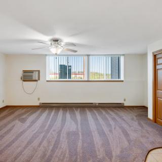 A spacious apartment room featuring large windows and a ceiling fan, ready for personalization.