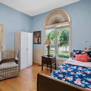 A cozy bedroom with blue walls, a floral bedspread, and large arched windows allowing natural light to fill the room.