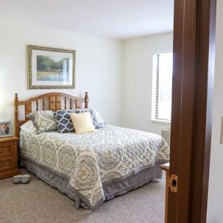 A cozy bedroom with a neatly made bed, wooden furniture, and a framed painting on the wall.