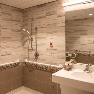 A modern bathroom featuring a sink, mirror, and tiled walls with an accessible shower.