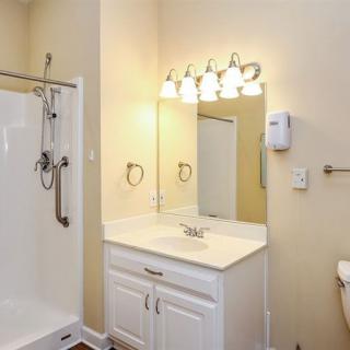 A clean and well-lit bathroom with a shower, vanity with a sink, mirror, and overhead lighting.