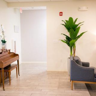 A minimalist waiting room with a piano, plant, and a gray sofa.