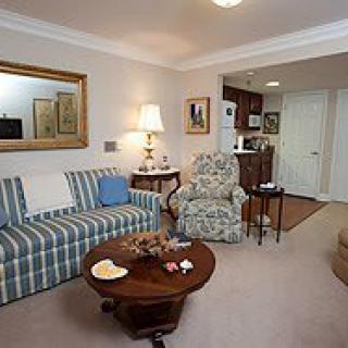 A cozy living room featuring a striped sofa, floral armchair, wooden coffee table, and decorative elements like a mirror and lamp.
