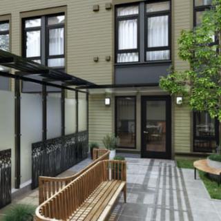 A modern courtyard featuring wooden benches, a tree, and sleek architectural elements.