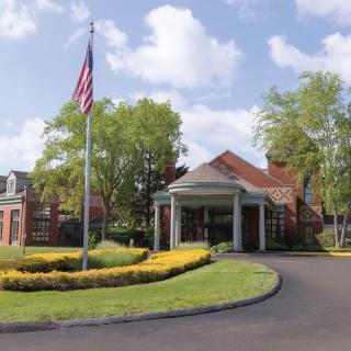 A brick building with a covered entrance, surrounded by lush landscaping and an American flag on a pole.
