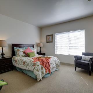 A cozy bedroom with a neatly made bed, chair, and bedside lamps.