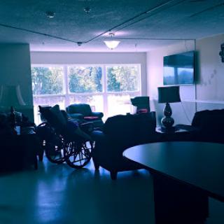 A cozy indoor living space featuring a wheelchair, comfortable seating, and ample natural light from large windows.