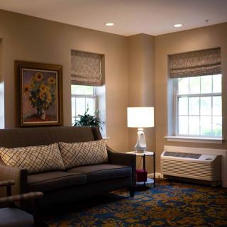 A cozy living room with a sofa, lamp, and artwork near large windows.