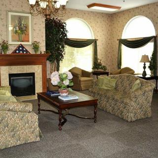 A cozy living room with classic decor, featuring floral sofas, a fireplace, and large arched windows.