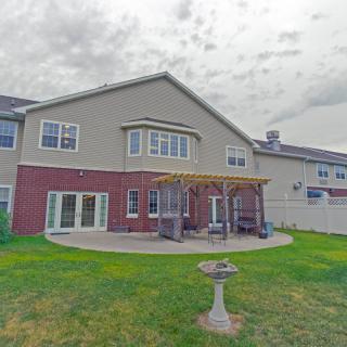 A two-story house with a brick and siding exterior, featuring a backyard patio with a pergola and a well-maintained lawn.