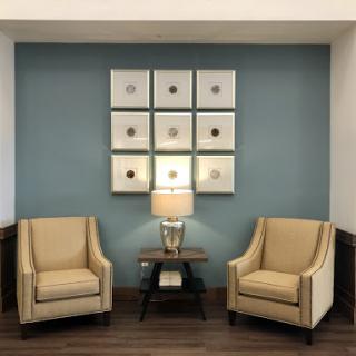 A cozy seating area featuring two beige chairs, a stylish lamp, and decorative wall art.