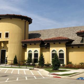 A view of a modern commercial building with Mediterranean-style architecture, featuring a curved facade and landscaped surroundings.
