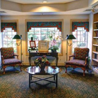 A cozy living room with elegant furniture, featuring chairs and a table centered between two large windows.