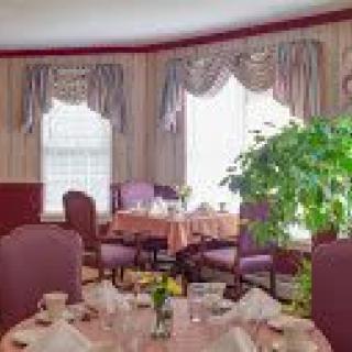 An elegantly decorated dining room with tables set for a meal, featuring windows with draped curtains and a large indoor plant.