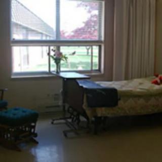 A hospital room with a bed, chair, and a window providing natural light.