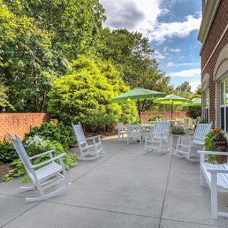 A peaceful patio area with white rocking chairs and a large umbrella, surrounded by lush greenery.