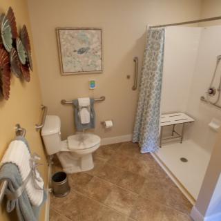 A well-organized bathroom featuring a shower with a bench, toilet, and neatly arranged towels.