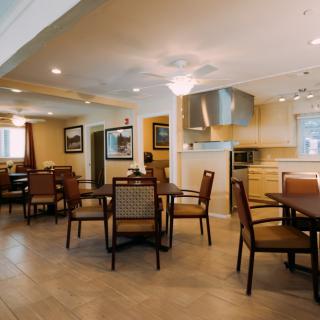 A spacious dining area with multiple tables and chairs, adjacent to a modern kitchen.