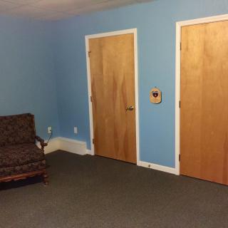 A simple room with blue walls, two wooden doors, and a piece of furniture on a carpeted floor.