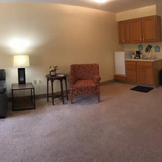 A cozy living room with an armchair, a small table, and a kitchenette.