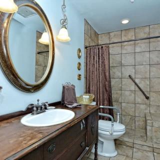 A well-appointed bathroom featuring a wooden vanity with a round mirror, tiled shower area, and modern fixtures.