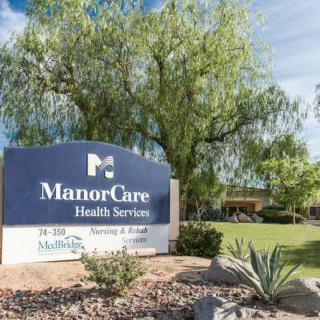 Sign for ManorCare Health Services surrounded by greenery.
