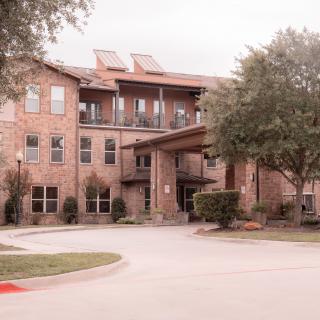 A residential building with a brick exterior, surrounded by trees and a driveway in front.