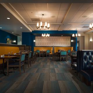 A modern restaurant interior featuring elegant chandeliers, a blue and yellow color scheme, and neatly arranged tables and chairs.