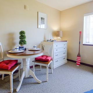 A cozy dining area with a round table, red-cushioned chairs, and white furniture bathed in natural light.