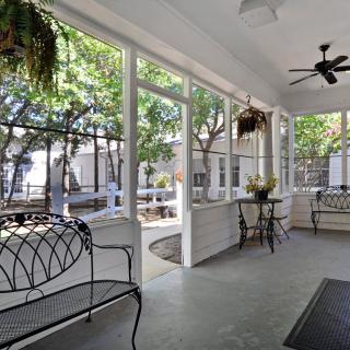 A cozy screened porch with outdoor seating, plants, and a ceiling fan overlooking a tree-filled backyard.