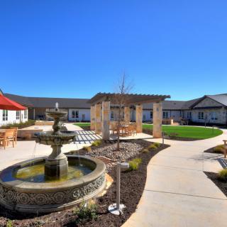 A tranquil courtyard featuring a central fountain, surrounded by modern buildings and landscaped walkways under a clear blue sky.