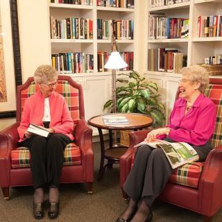 Two seniors enjoy a conversation in a cozy library setting, surrounded by books.